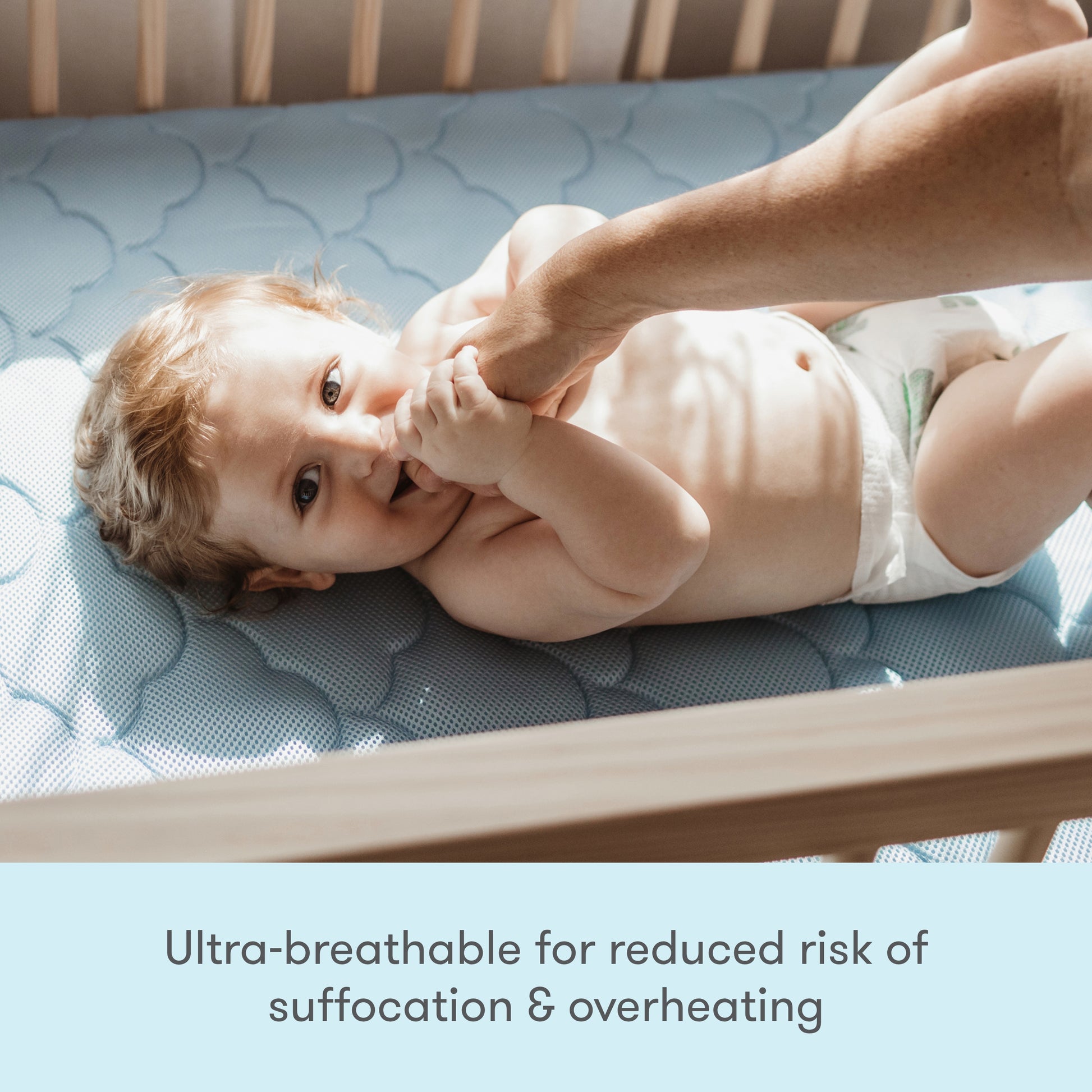 Image of a baby wearing a cute outfit, lying on a mattress, with text stating "Ultra breathable for reduced risk of suffocation & overheating."