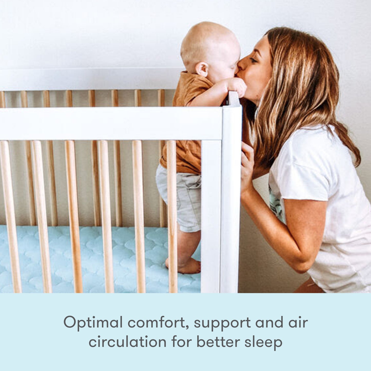 mother holding baby and kissing it while baby stands on blue newton mattress with text "optimal comfort support and air circulation for better sleep"