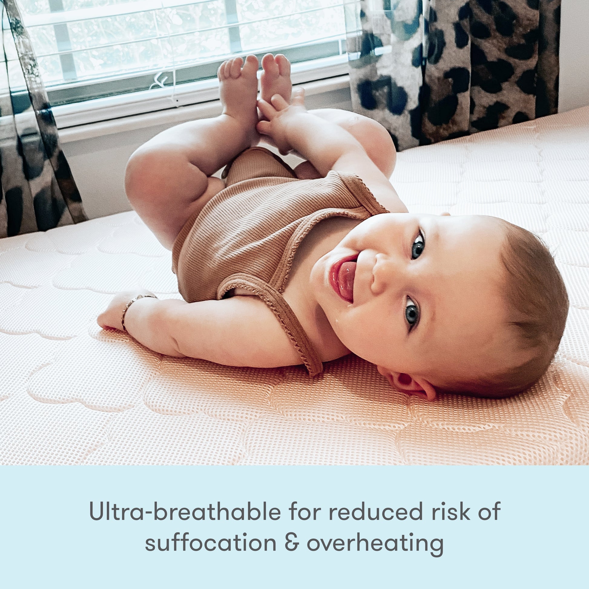 Image of a baby wearing a cute outfit, lying on a mattress, with text stating "Ultra breathable for reduced risk of suffocation & overheating."