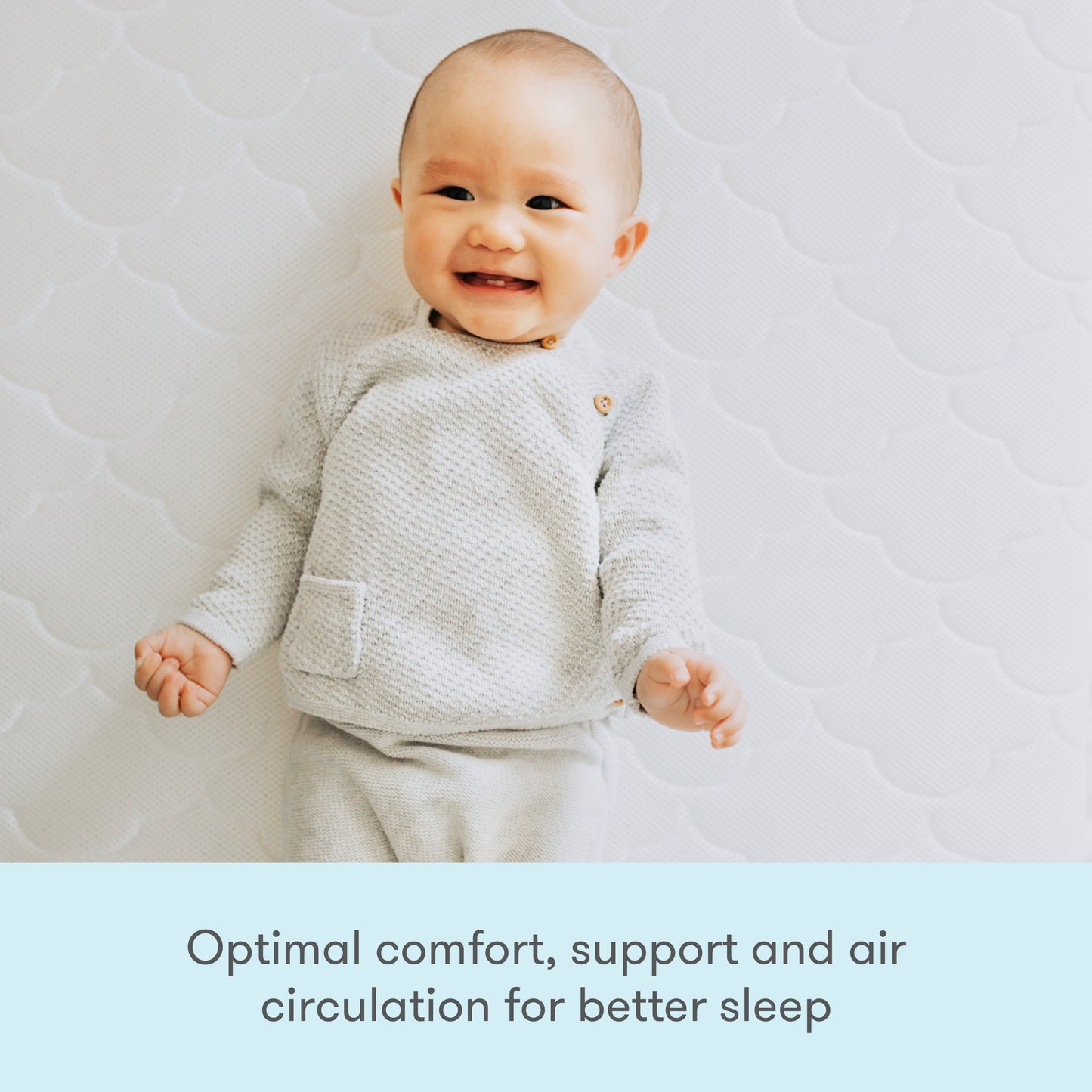 A smiling baby lying on a light-patterned background, wearing a textured light gray outfit, with the text "Optimal comfort, support, and air circulation for better sleep" on the left side.
