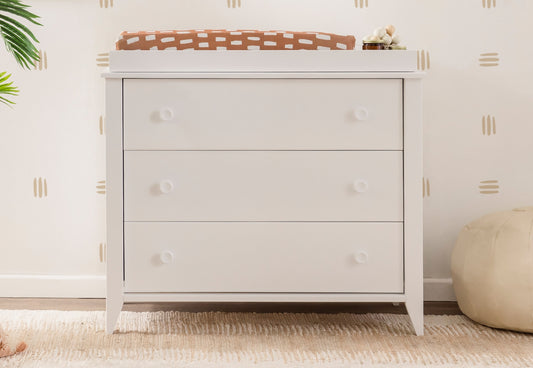 Modern white three-drawer dresser with a neutral-toned, patterned changing pad on top, set against a softly decorated nursery wall. 999-8603-WHT