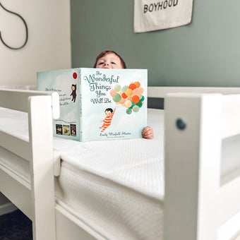 A child relaxes on a luxurious Newton mattress, captivated by the book "The Wonderful Things You Will Be."