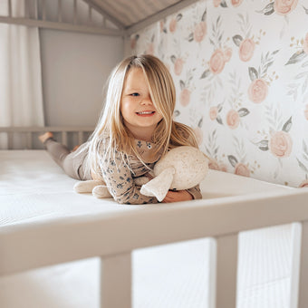 A little girl peacefully lays in her crib, cuddling a soft stuffed animal.