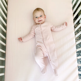 A baby in a pink sleeper peacefully lying on a soft bed