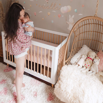A woman gently holds her baby in a crib, creating a warm and nurturing atmosphere.