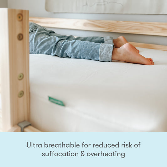 A child lies on their side on a plain white mattress with wooden bed rails. Text below reads: Newton Baby Waterproof Organic Twin Mattress Pad—ultra breathable for less risk of suffocation and overheating.