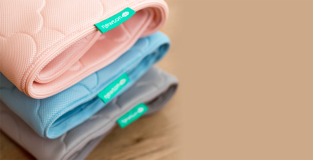 Three colorful Newton Crib Mattress Cover neatly arranged on a khaki color background, showcasing vibrant hues and soft textures.