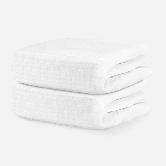 Two neatly stacked white cotton baby blankets on a solid white background. skip
