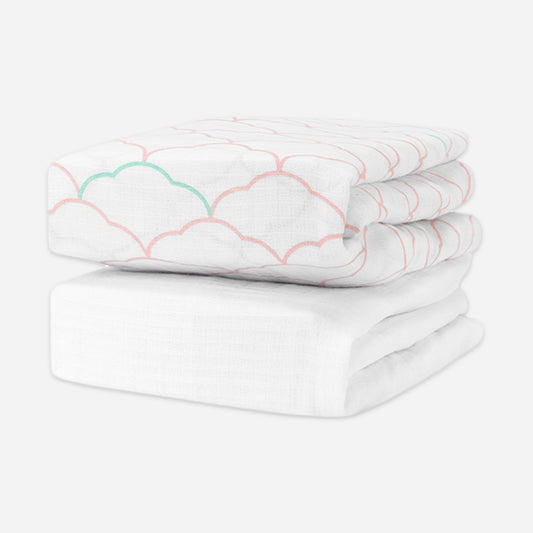 A stack of baby crib sheets with cloud patterns in orange and green outlines, atop a plain white crib sheet. skip