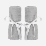 Two rolled-up light gray Travel Crib & Play Yard Sheets, each tied with a white satin ribbon, are placed side by side on a plain white background.