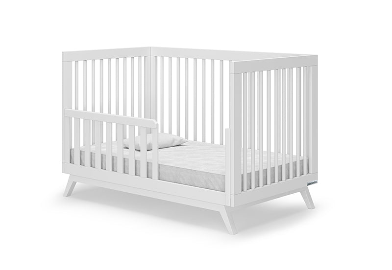 The dadada baby Soho Convertible Crib is a modern white 3-in-1 crib with slatted sides, a partial guardrail, mattress, and pillow, shown against a plain white background.