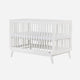 The dadada baby Soho Convertible Crib is a white wooden 3-in-1 crib with slatted sides, mid-century style, and four angled legs. It comes with a white Newton crib mattress for comfort.