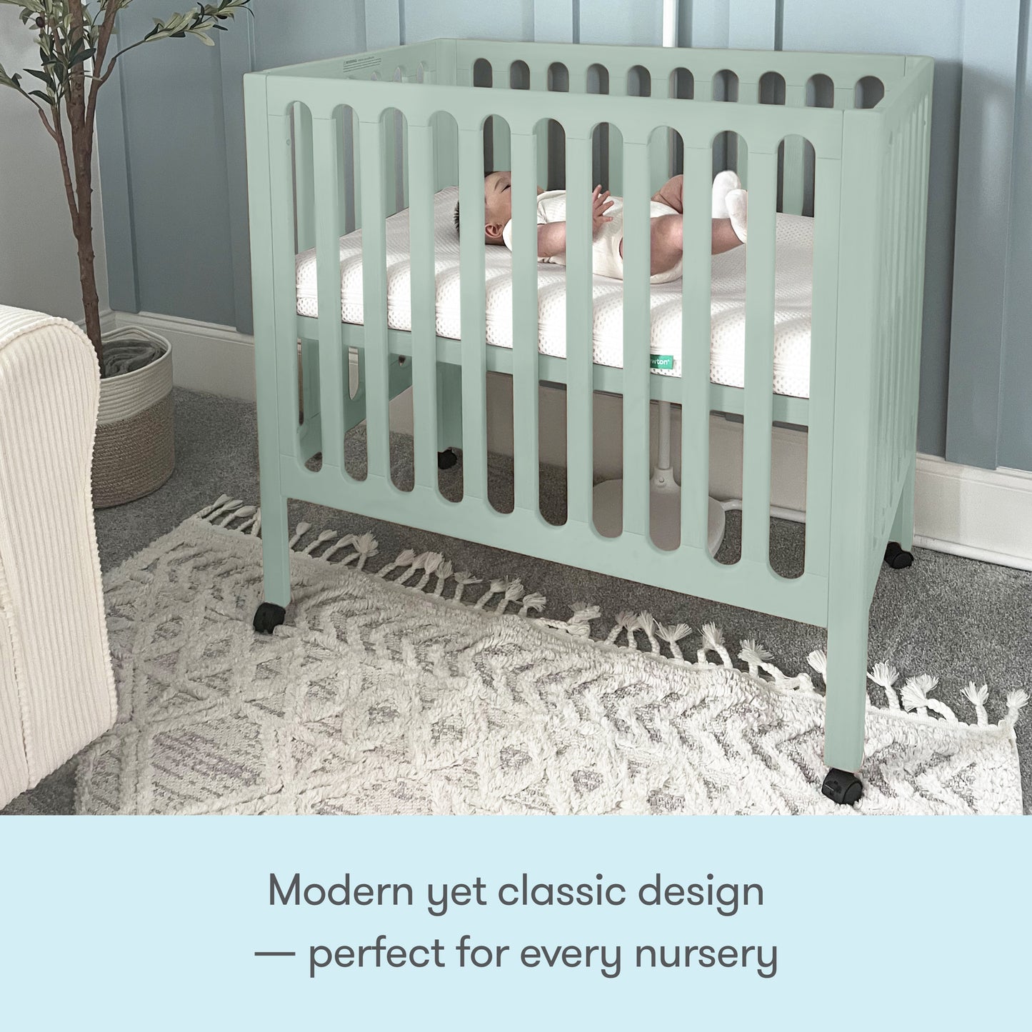 A baby lies in a mint green Newton Galileo Mini Crib with Newton Mattress by Newton Baby, featuring vertical slats, on a patterned rug in a softly lit nursery. Text below reads: Modern yet classic design—perfect for every nursery.