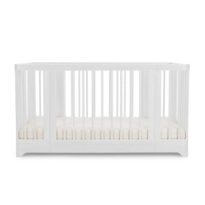 The Newton Nest Convertible Crib by Newton Baby is a modern white 4-in-1 crib with vertical slats on all sides and includes a plain, light-colored mattress. GREENGUARD Gold certified, it provides a safer sleep environment for your baby. The crib is set against a plain white background.