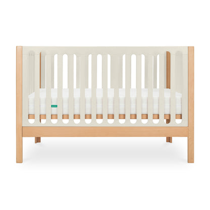 The Newton Galileo Convertible Crib by Newton Baby features natural beech wood legs and frame, white slatted sides, a white mattress, and a minimalist design. It converts to a toddler bed for long-lasting versatility.