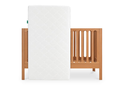 White crib mattress with a scalloped pattern standing next to a wooden crib on a white background.