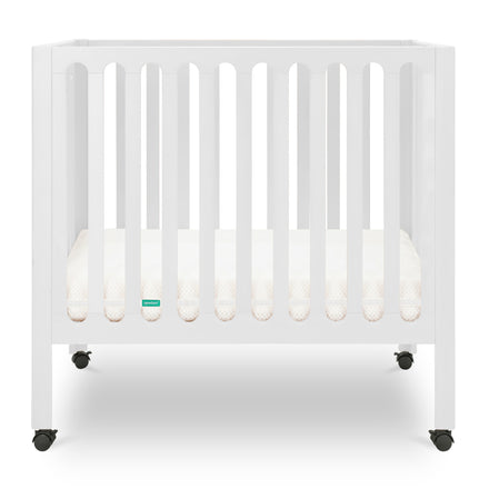 White modern baby crib with a thin mattress on wheels. skip