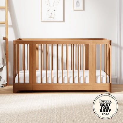 A Newton Baby Newton Nest Convertible Crib with vertical slats and a striped mattress sits in a softly lit nursery. Animal art hangs above, and the crib features GREENGUARD Gold certification and a Parents Best for Baby 2026 award badge. 999-8442-CST-C1