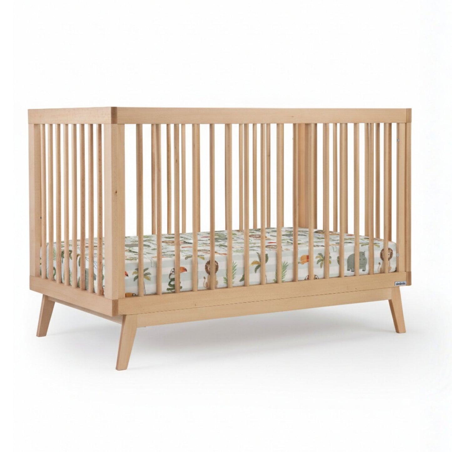 The dadada baby Soho Convertible Crib is a modern 3-in-1 crib with vertical slats, angled legs, and mid-century design. Shown with a fitted mattress and colorful animal and nature-themed bedding against a plain white background. 500-8220-NAT