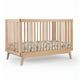 The dadada baby Soho Convertible Crib is a modern 3-in-1 crib with vertical slats, angled legs, and mid-century design. Shown with a fitted mattress and colorful animal and nature-themed bedding against a plain white background. 500-8220-NAT