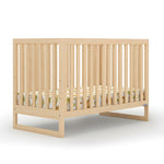 The dadada baby Austin Convertible Crib, made from sustainable beechwood with vertical slats and a colorful patterned mattress, is shown in light wood against a white background.