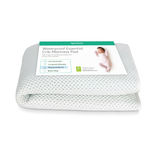 A folded Newton Baby Essential Waterproof Crib Pad with a breathable white and gray dotted design, shown with its product label and a picture of a sleeping baby.