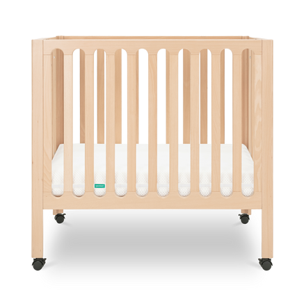 A wooden baby crib with vertical slats and four wheels, shown on a white background. The crib has a light natural wood finish and a white mattress inside.