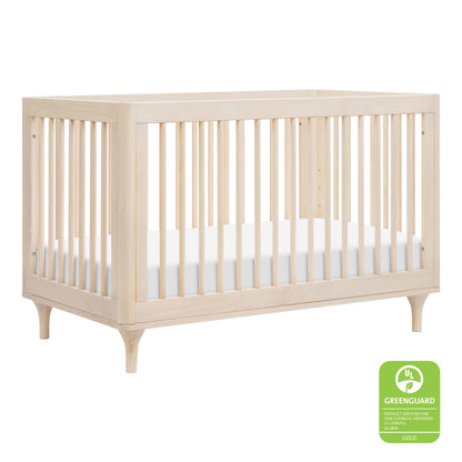The Babyletto Lolly Convertible Crib, made from New Zealand pine wood, features vertical slats, a white mattress, mid-century modern legs, and a Greenguard Gold certification label in the lower right corner.
