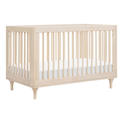 The Babyletto Lolly Convertible Crib features a modern design with slatted New Zealand pine sides, slightly tapered legs, a white mattress, and convertible functionality.