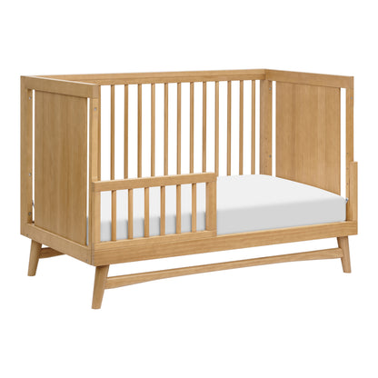 The Babyletto Peggy Convertible Crib features a light wood frame, open slats on two sides, solid head and foot panels, and a white mattress—perfect for a modern nursery.