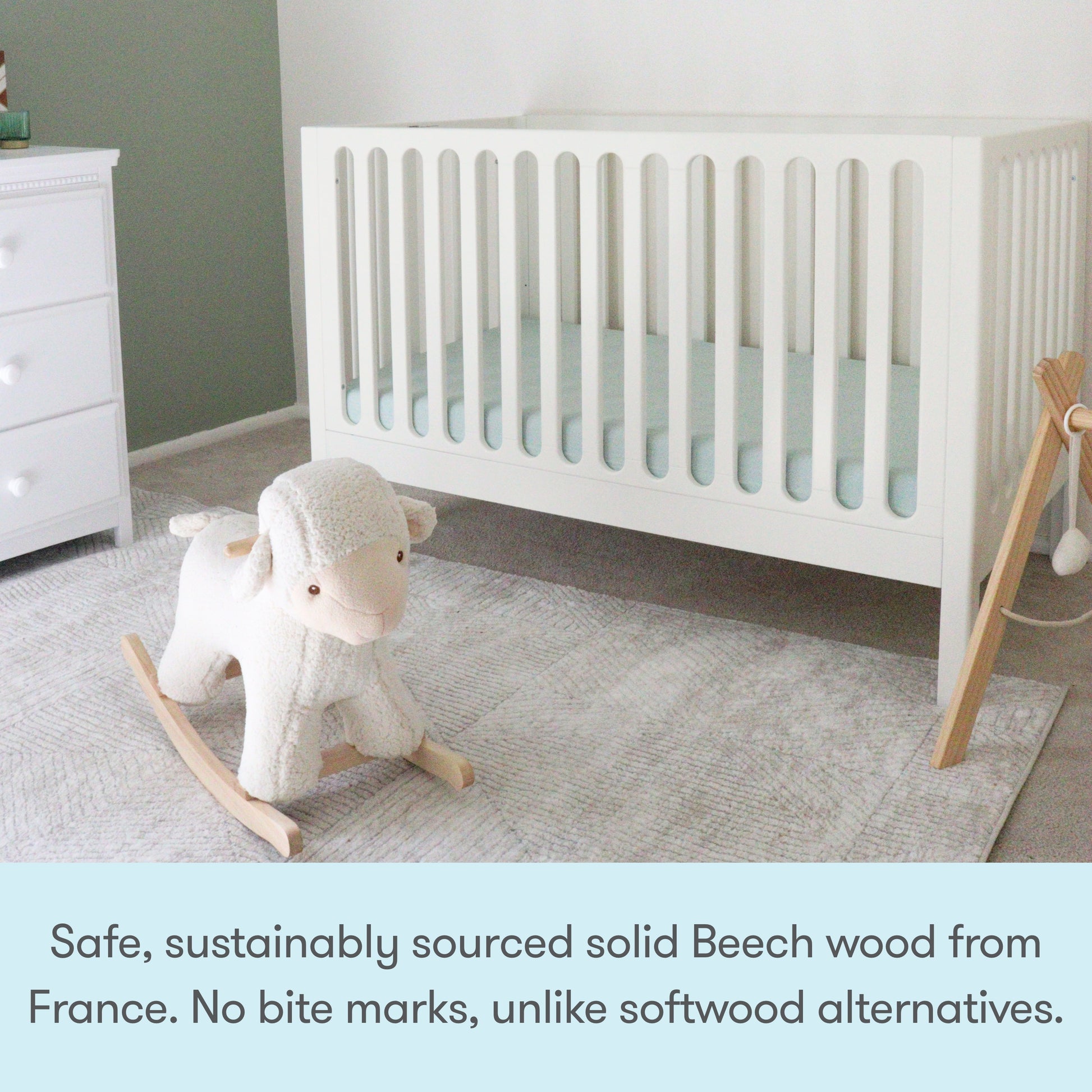The Newton Galileo Convertible Crib by Newton Baby, crafted from solid French Beech, features vertical slats and converts easily to a toddler bed. Shown on a light gray rug beside a dresser with a plush sheep rocker. Safe, sustainable, and no bite marks!.