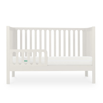 The Newton Galileo Convertible Crib by Newton Baby features white beech wood, vertical slats, an open side with a toddler rail, and a white mattress that showcases its toddler bed conversion against a plain white background.
