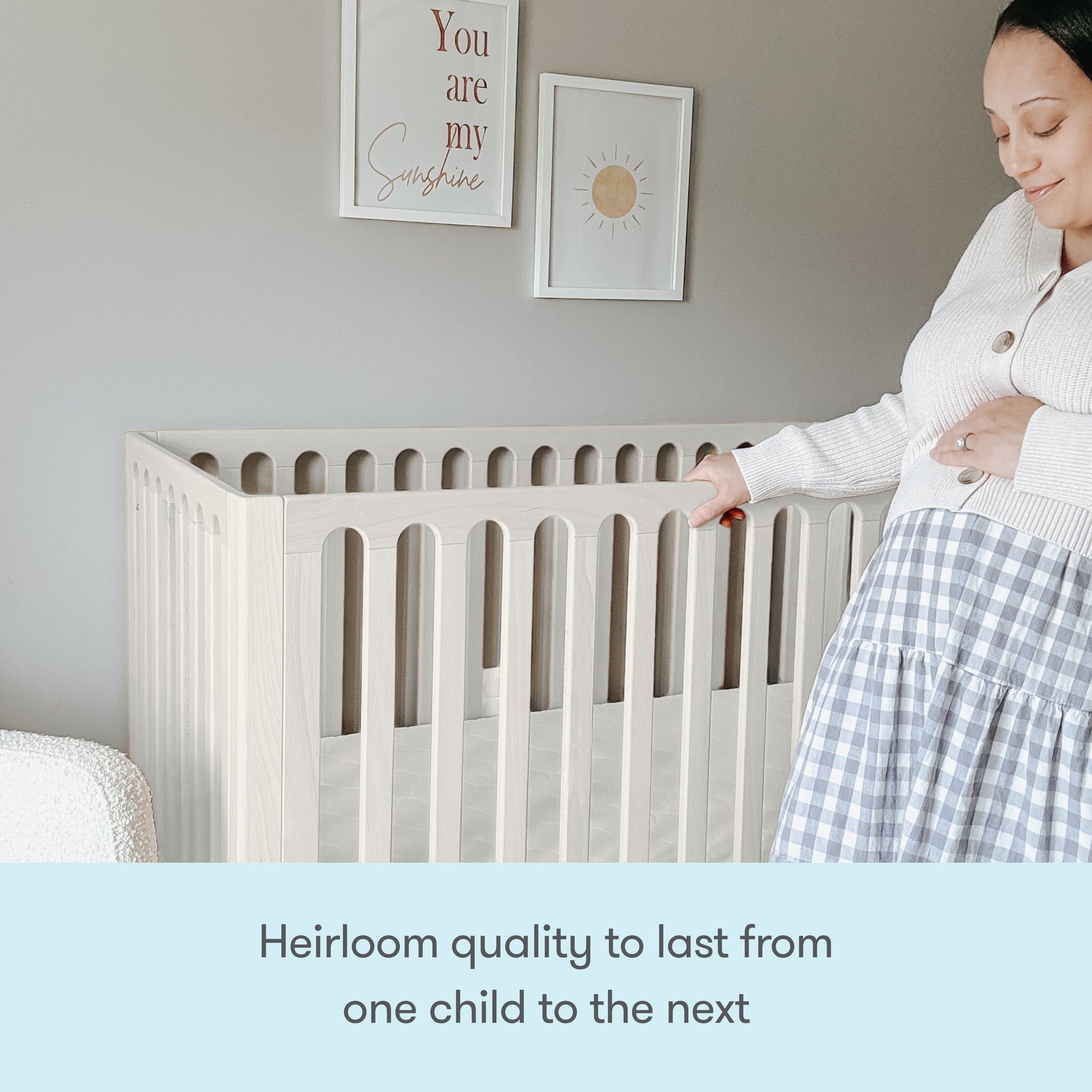 A pregnant woman stands beside the Newton Galileo Convertible Crib by Newton Baby in a softly decorated nursery, smiling and touching her belly. Text below reads: Heirloom quality with toddler bed conversion for growing families.