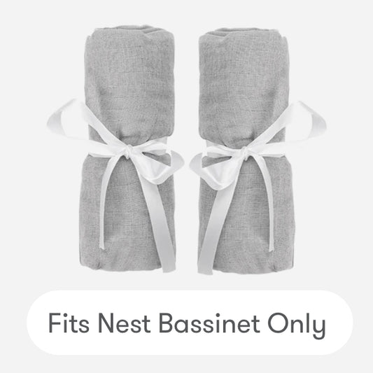 Two gray cotton muslin Nest Bassinet Extra Sheets by Newton Baby, rolled and tied with white ribbons, side by side on a light background. Text below: Fits Nest Bassinet Only—perfect breathable crib sheets for your baby.