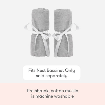 Two rolled-up light gray Newton Baby Nest Bassinet Extra Sheets are tied with white ribbons. These pre-shrunk, machine-washable cotton muslin crib sheets fit the Nest Bassinet (sold separately) and offer breathable comfort.
