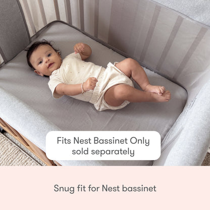 A baby lies in a light gray Nest Bassinet. Text reads, “Newton Baby Nest Bassinet Extra Sheets—fits snugly, compatible with cotton muslin and breathable crib sheets. For use with Nest Bassinet only (sold separately).”.