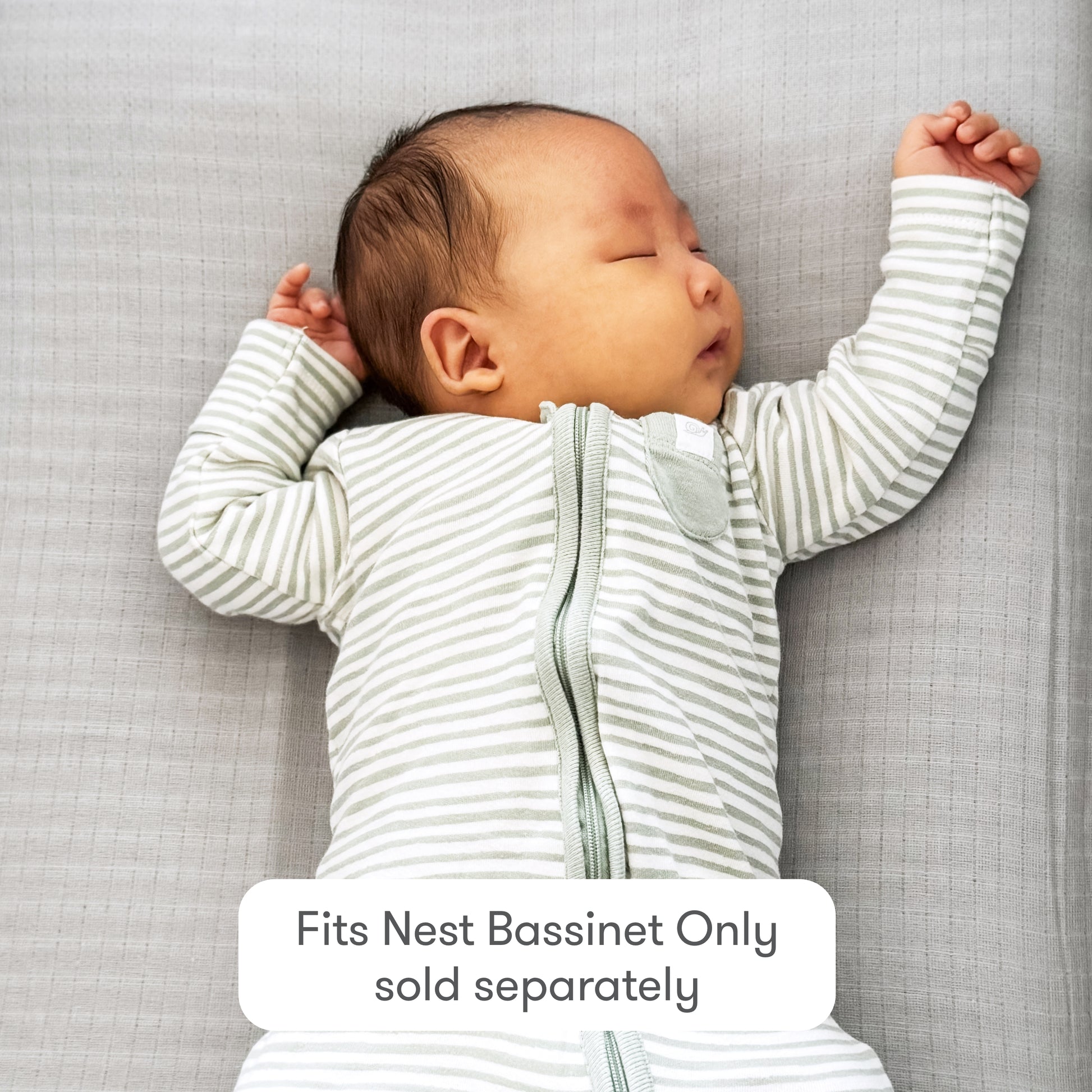 A baby in a gray and white striped onesie sleeps on a light gray surface, arms raised. Text overlay: Newton Baby Nest Bassinet Extra Sheets—cozy cotton muslin, breathable comfort. Fits Nest Bassinet only; bassinet sold separately.