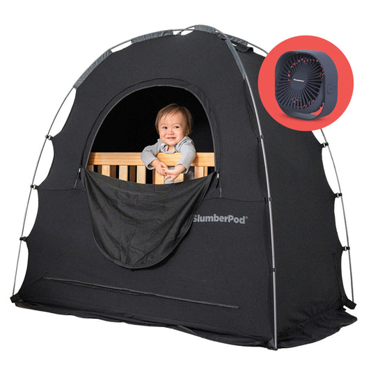 Baby in crib peeking out through window into slumberpod tent, big black tent over wooden crib with baby inside. Icon with portable fan indicating product comes with additional portable fan.