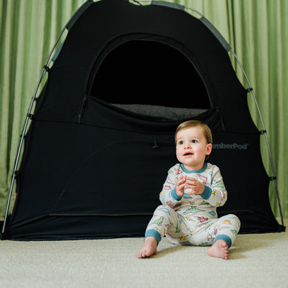 baby sitting in front of slumberpod tent with a green curtain behind