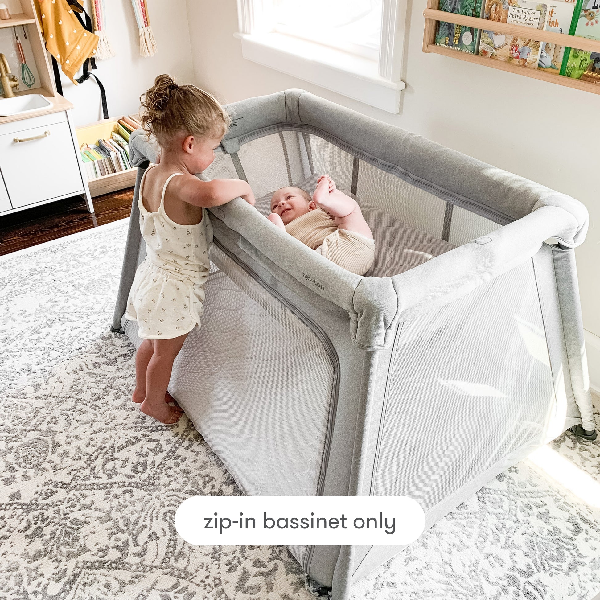 toddler standing next to play yard looking at baby laying in bassinet insert with text "zip-in bassinet only", Bassint Only