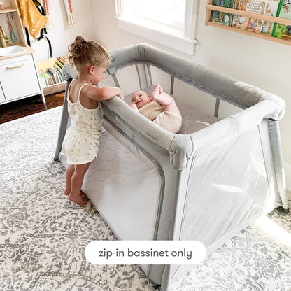 toddler standing next to play yard looking at baby laying in bassinet insert with text "zip-in bassinet only", Bassint Only