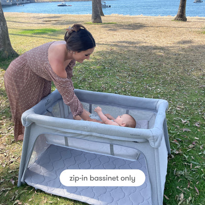 Mother placing baby in bassinet insert outdoors, with text, "zip-in bassinet only", Bassinet Only