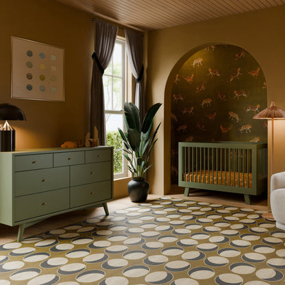 A stylish nursery featuring green furniture, a Babyletto Hudson Convertible Crib and dresser, a patterned rug, tall plant, window with gray curtains, and charming animal illustration wallpaper behind the crib.
