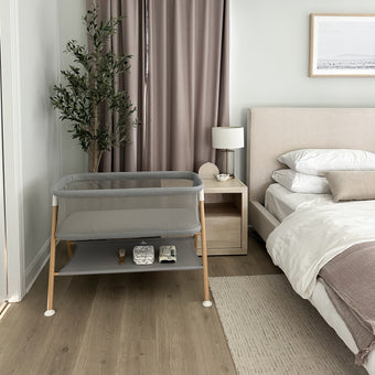 Essential Bassinet in gray in mutual room  with storage shelf and faux wood legs 