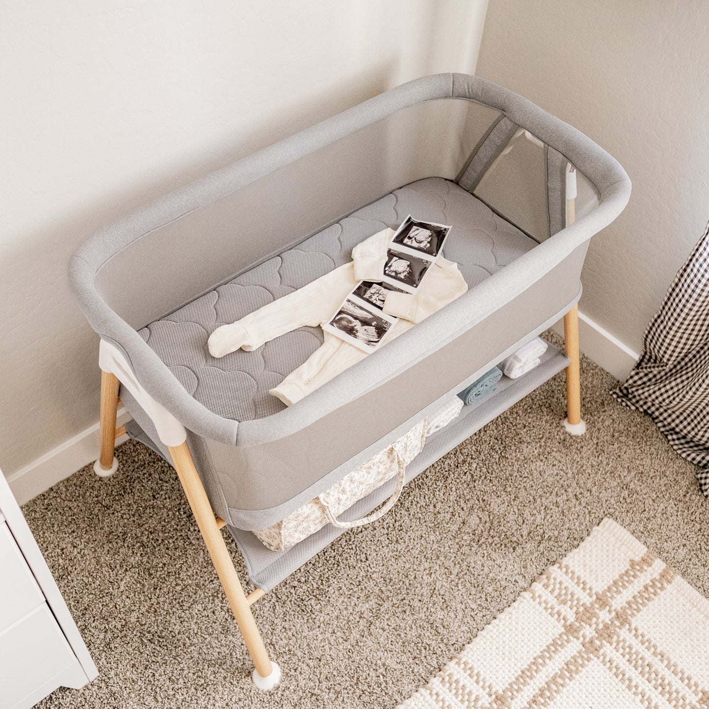 cream onesie with sonogram image on gray bassinet mattress in essential bassinet in a neutral toned room
