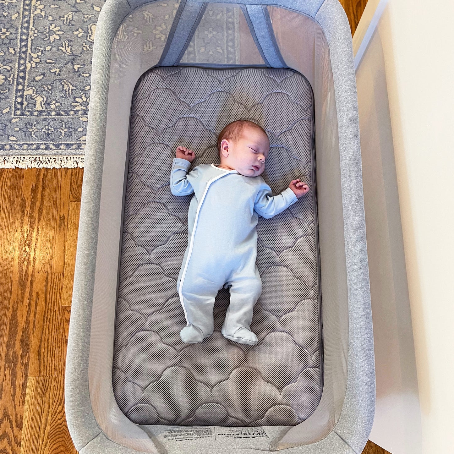 Sleeping baby in gray onesie on gray cloud pattern bassinet mattress for essential bassinet