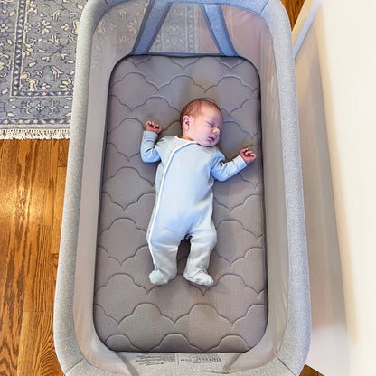 Sleeping baby in gray onesie on gray cloud pattern bassinet mattress for essential bassinet