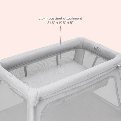 The Newton Baby Deluxe Travel Crib & Play Yard is shown with a light gray zip-in bassinet and mesh sides, featuring a breathable mattress (31.5 x 19.5 x 8), against a pale pink background.
