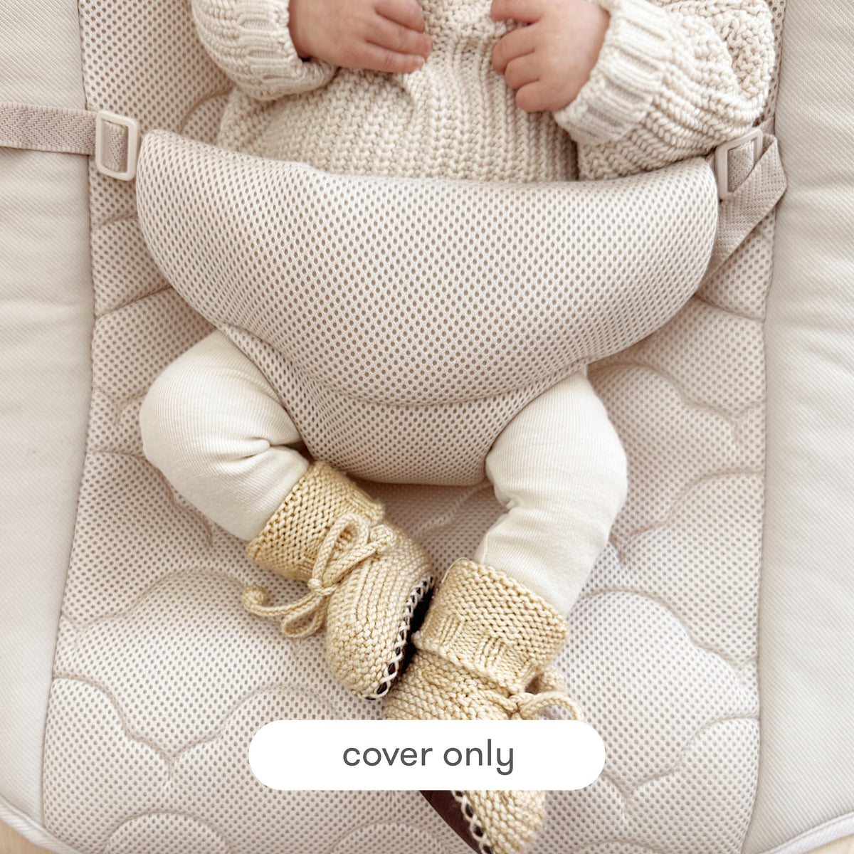 A baby, dressed in a sweater and knitted boots, sits in a cushioned beige Newton Baby rocker featuring the Baby Rocker Extra Cover. Text at the bottom reads “cover only.” Only the lower part of the baby’s face and body are visible.
