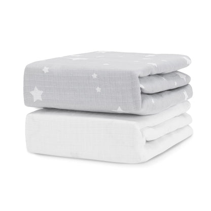 Two Newton Baby Breathable, Organic Cotton Sheets (2-pack) are stacked; the top is light gray with white stars and moons, while the bottom is solid white.